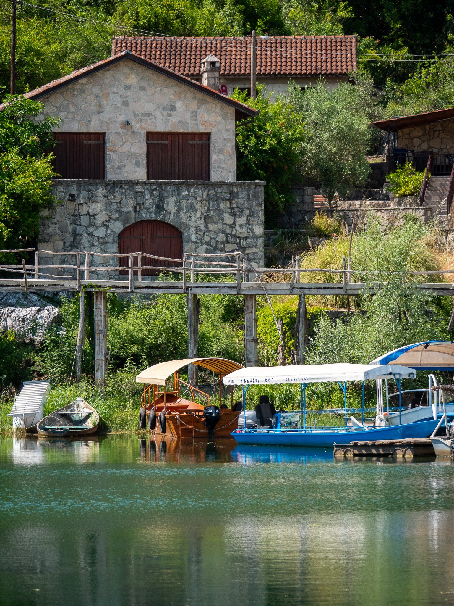 Maison en pierre, passerelle en bois et barques au bord du lac de Skadar à Karuč